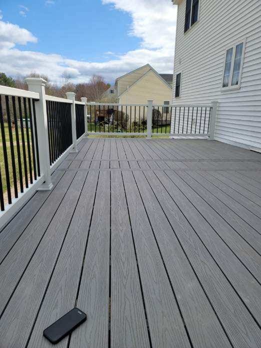 A gray deck with a white railing and a cell phone on it - Plaistow, NH - Dynamic Deck Solutions