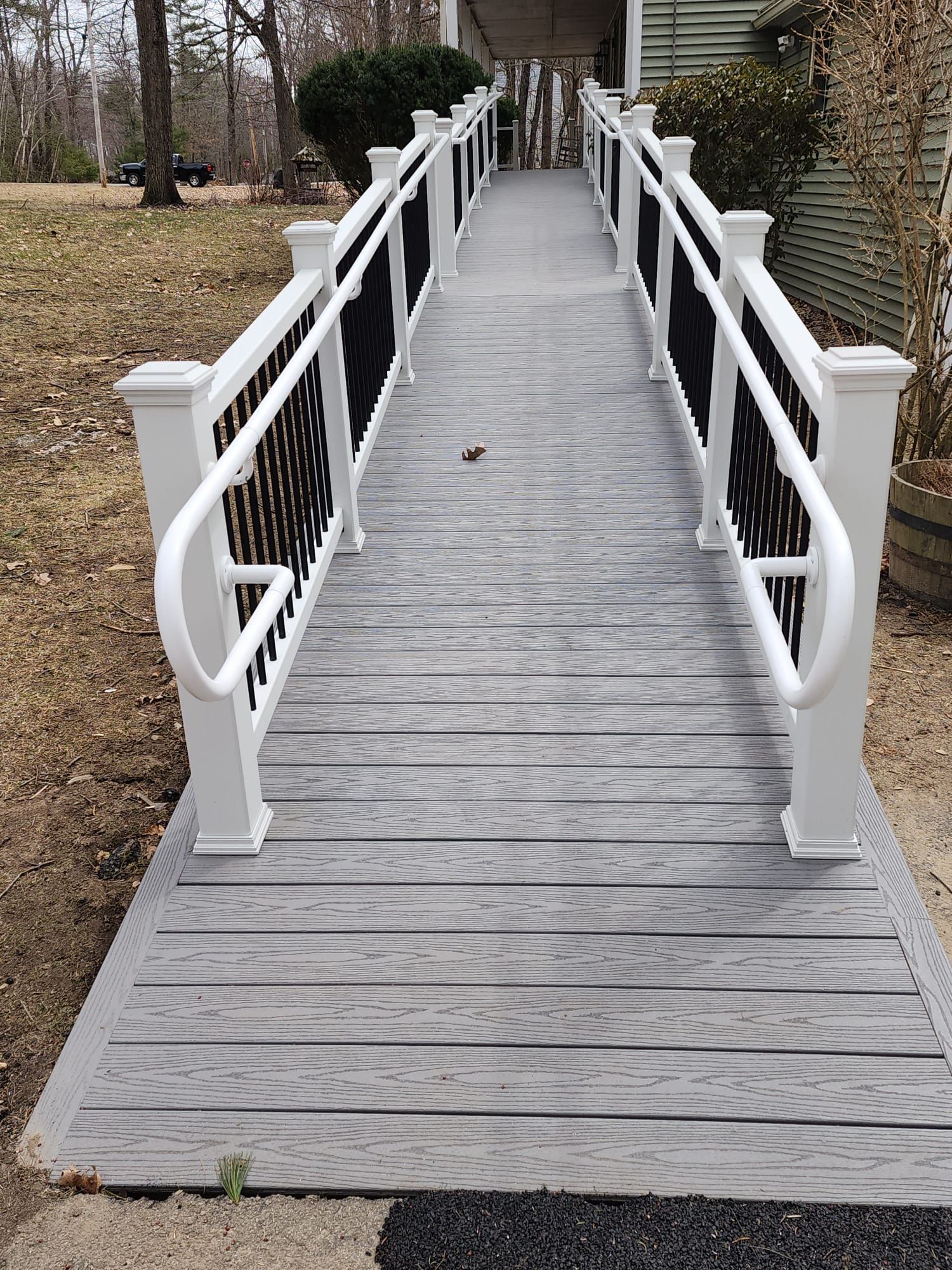 A wooden ramp with a white railing leading to a house - Plaistow, NH - Dynamic Deck Solutions