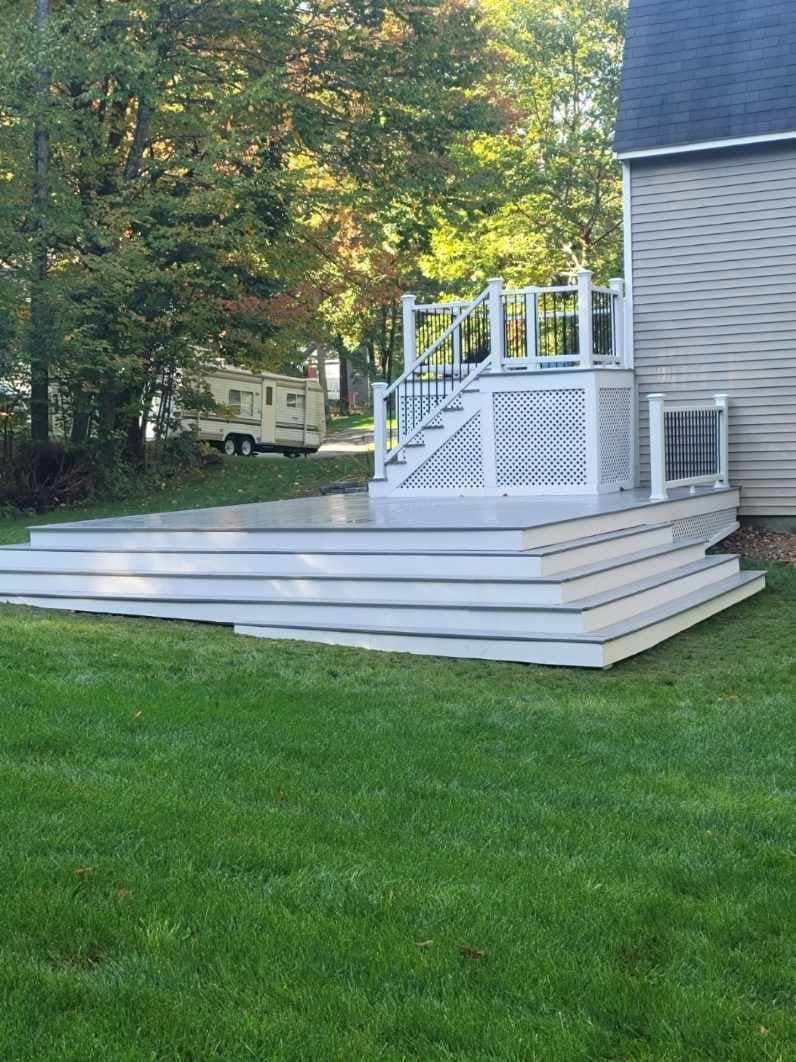 A white deck with stairs leading up to it is in the backyard of a house - Plaistow, NH - Dynamic Deck Solutions