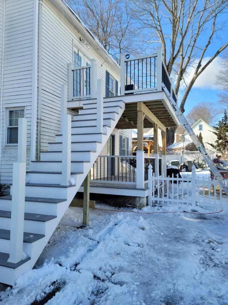 A white house with stairs leading up to a deck in the snow - Plaistow, NH - Dynamic Deck Solutions