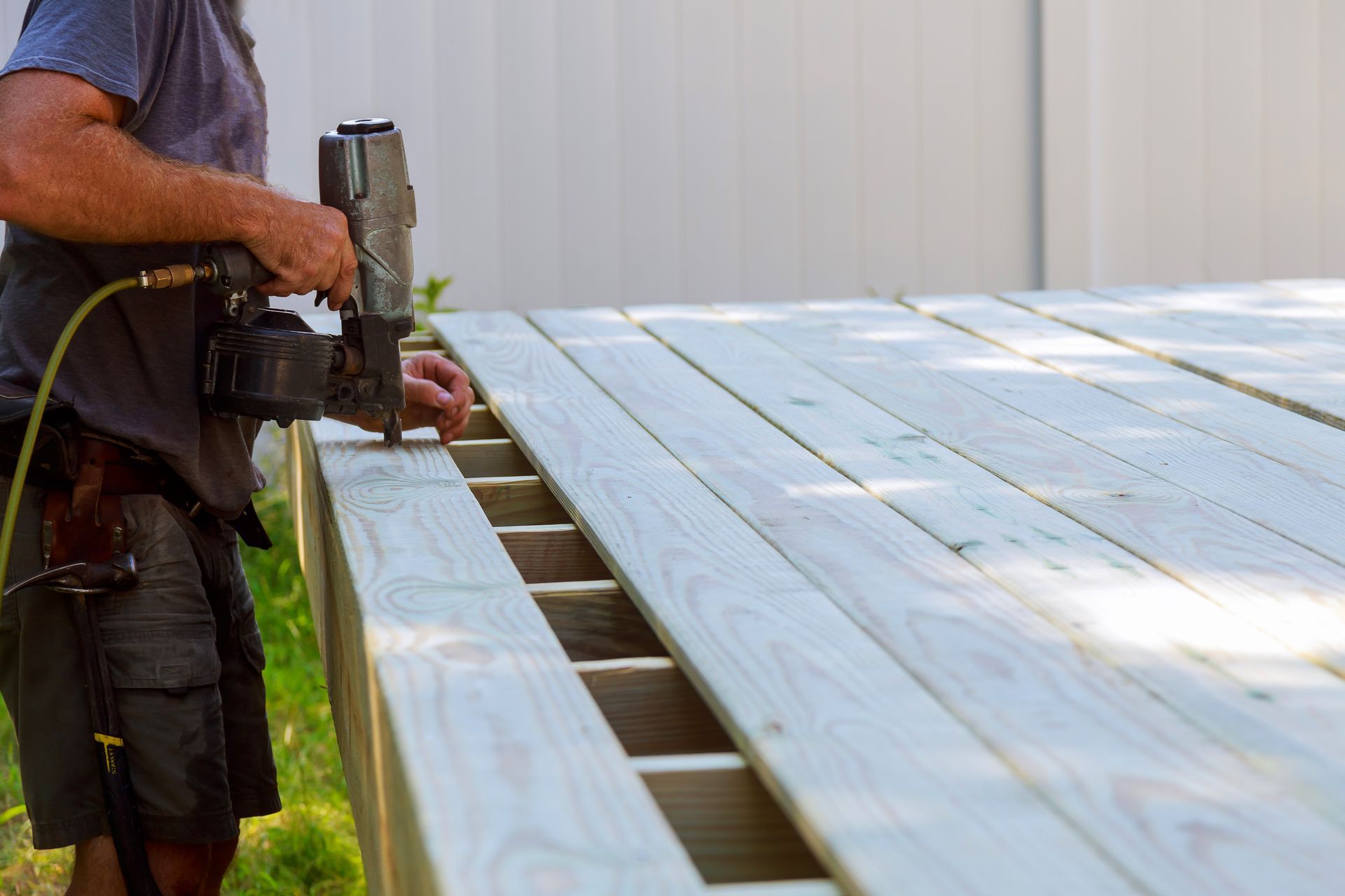 Person using a nail gun to install wooden boards on a deck frame outdoors. Person using a nail gun to install wooden boards on a deck frame outdoors.