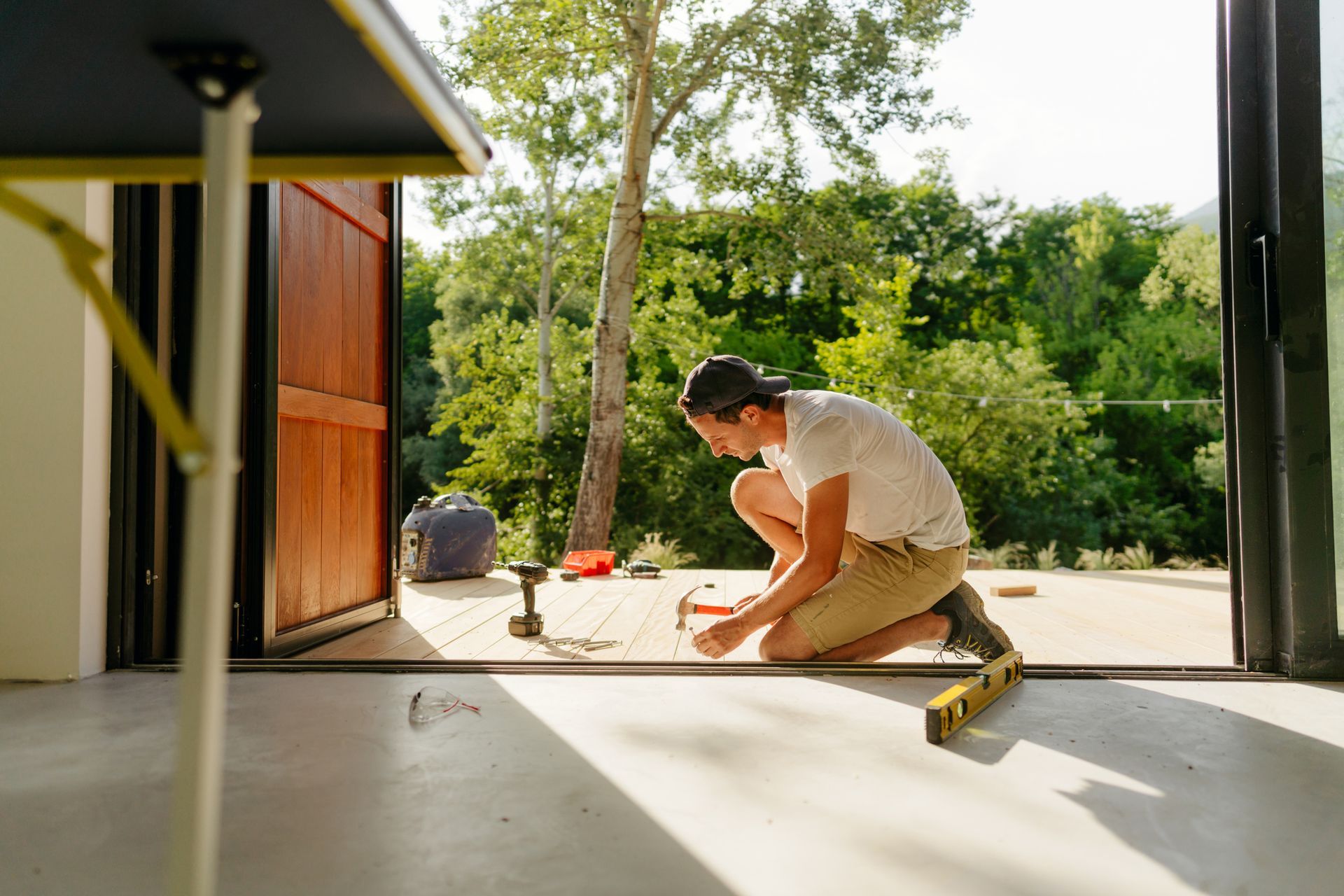 A man uses a hammer to work on a deck, focused on tasks related to deck construction services. A man uses a hammer to work on a deck, focused on tasks related to deck construction services.