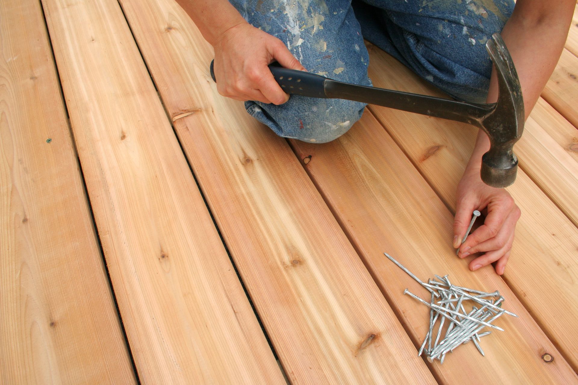 A person is hammering nails into a wooden deck. - Plaistow, NH - Dynamic Deck Solutions