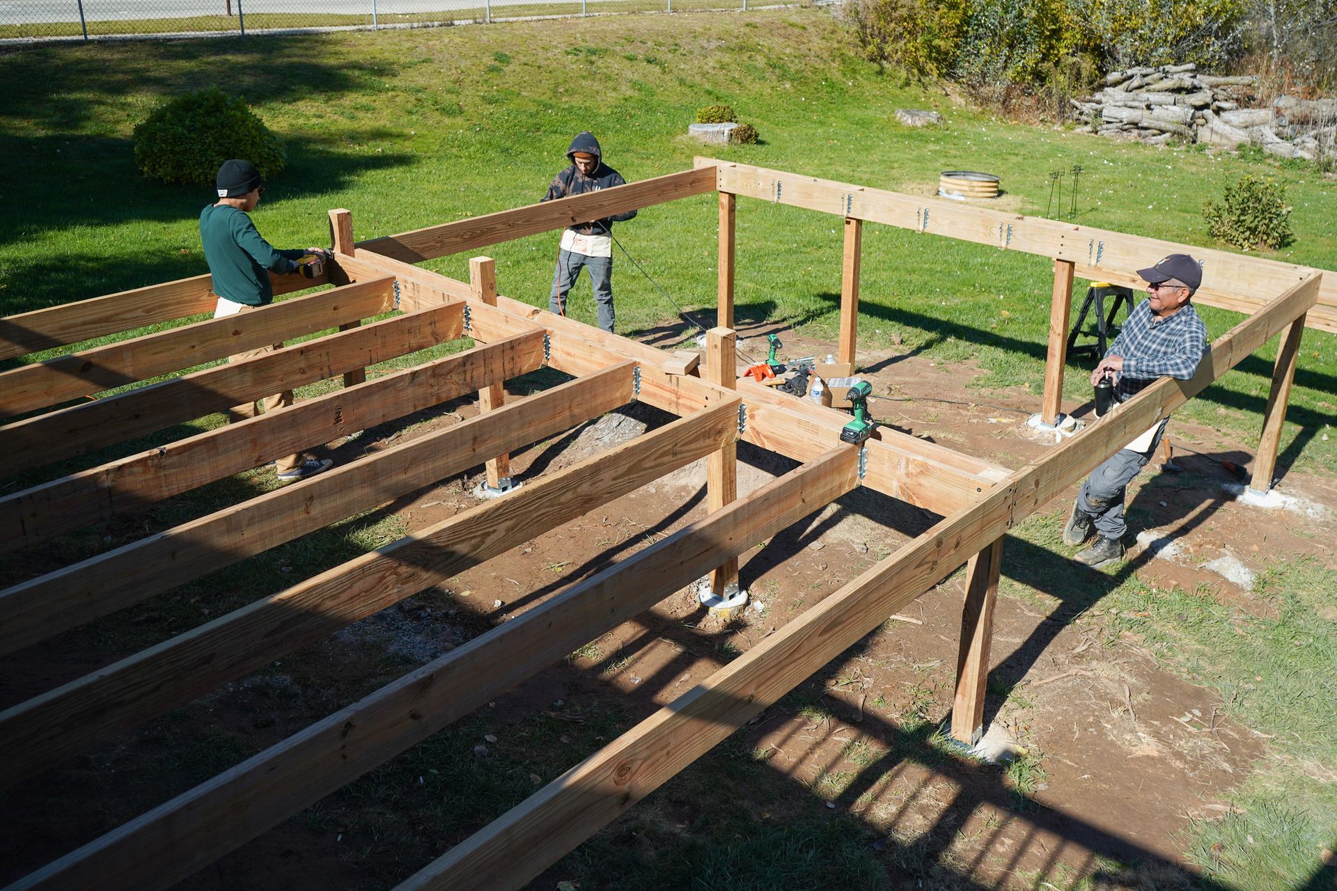 Professional deck builder team constructing wooden deck frame on residential backyard.