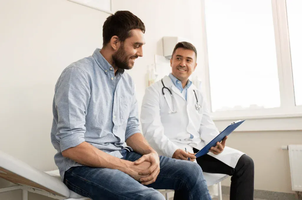 A man is sitting on a bed talking to a doctor.