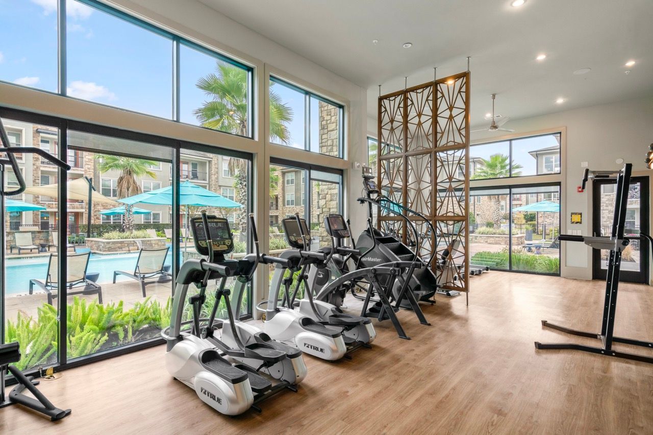 Indoor fitness center with treadmills and ellipticals by large windows overlooking the pool.