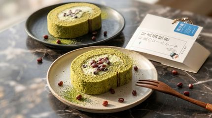 Green matcha roll cakes on dark plates with berries and a white dessert box on a gray table