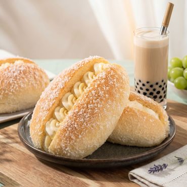 Cream-filled sugar-coated buns on a plate beside a milk tea with tapioca pearls and green grapes