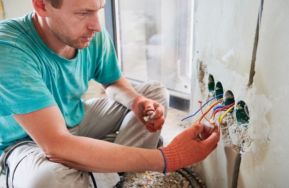 A man is sitting on the floor working on an electrical outlet.