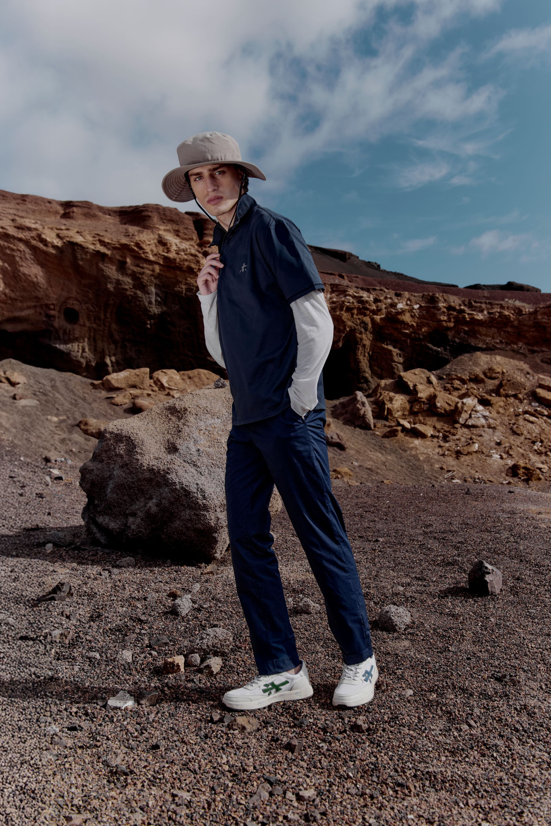 Persona in posa accovacciata, con indosso un berretto giallo, su un tetto con lo skyline della città sullo sfondo.