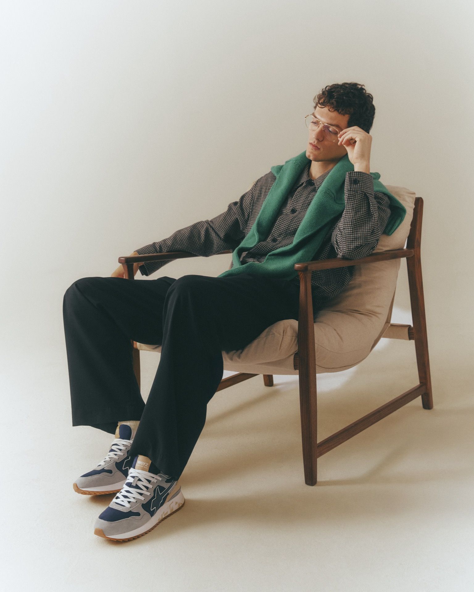 Un uomo con pantaloni arancioni e maglietta scura è accovacciato, mentre si allaccia una scarpa. Sullo sfondo si vede una struttura metallica colorata.