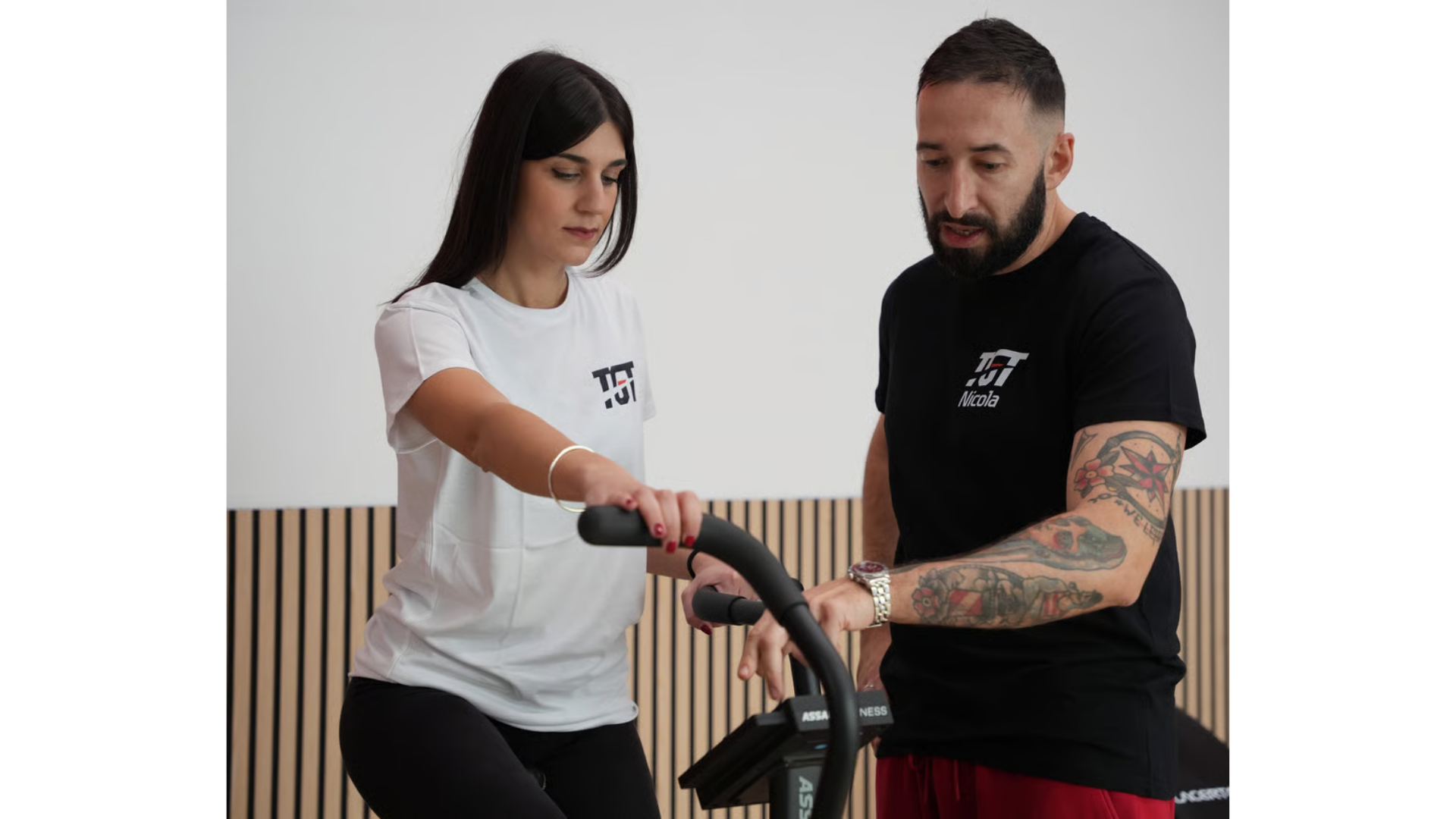 Un istruttore  impartisce istruzioni a una persona che utilizza un attrezzo ginnico fisso in una palestra.