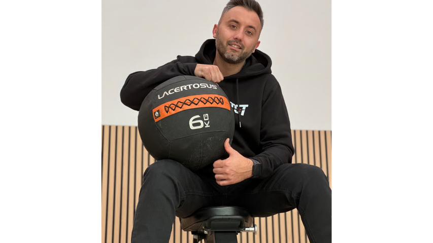 Una persona con una felpa nera con cappuccio è seduta su una panchina, sorridente, 