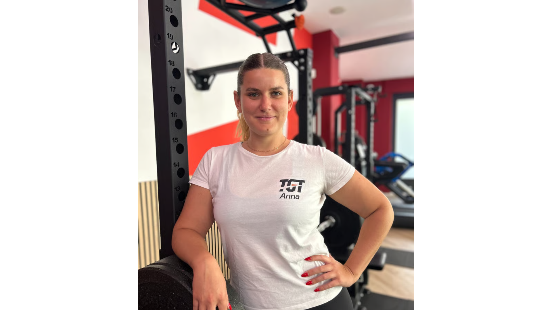 Una persona in piedi in una palestra, accanto a un bilanciere nero per squat, 