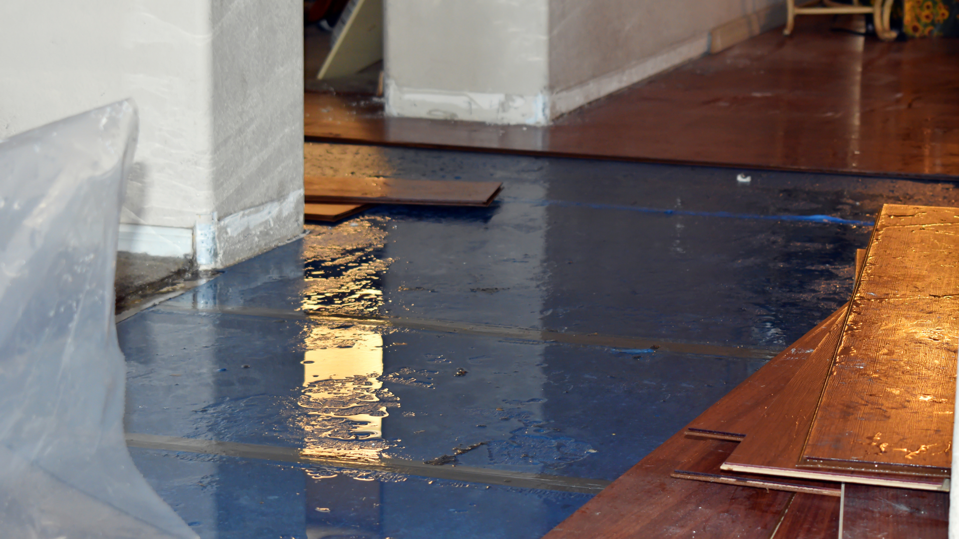 Flooded blue-tiled floor with water damage. Brown boards and white walls are visible in a dimly lit indoor space.