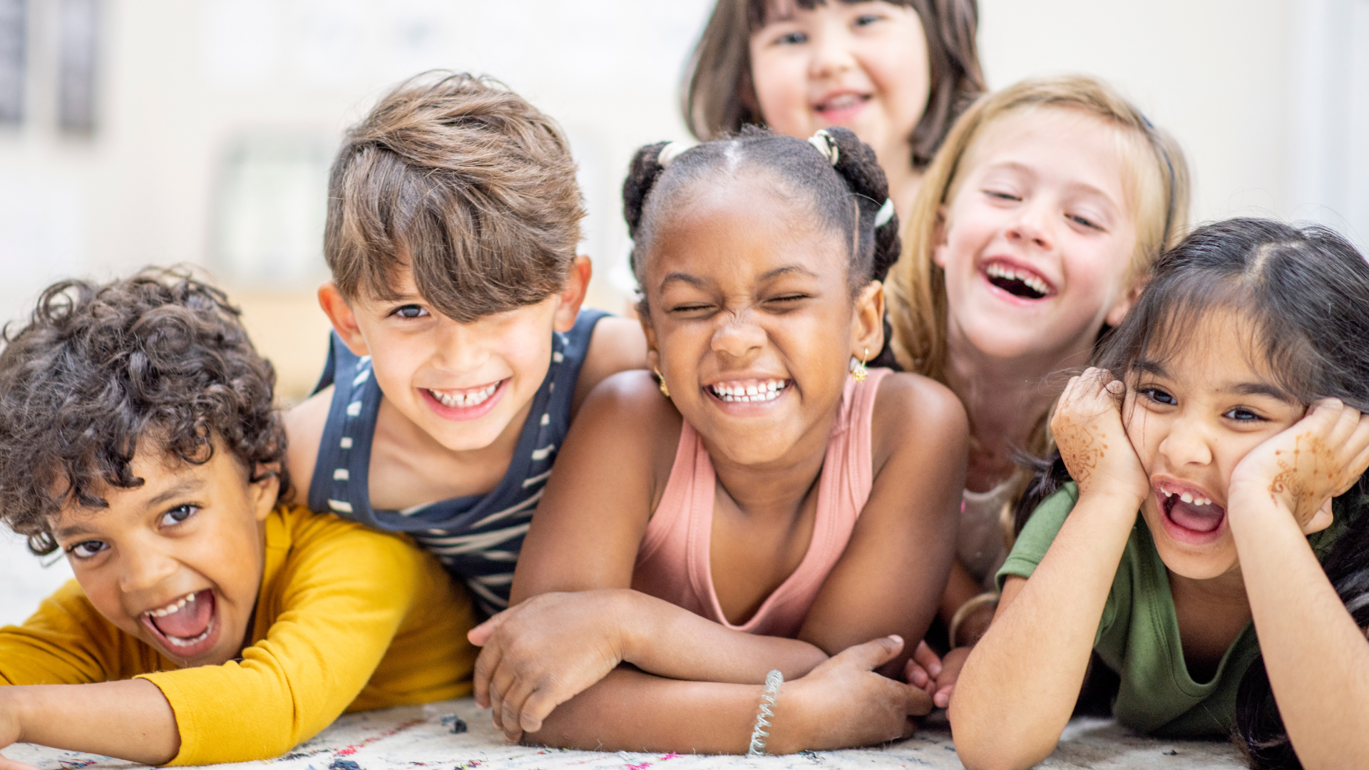 A group of children are laying on the floor together and smiling.