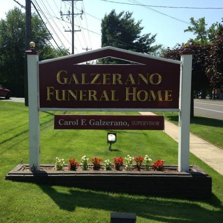 Sign for Galzerano Funeral Home; red and gold lettering, with a lawn and flowers.