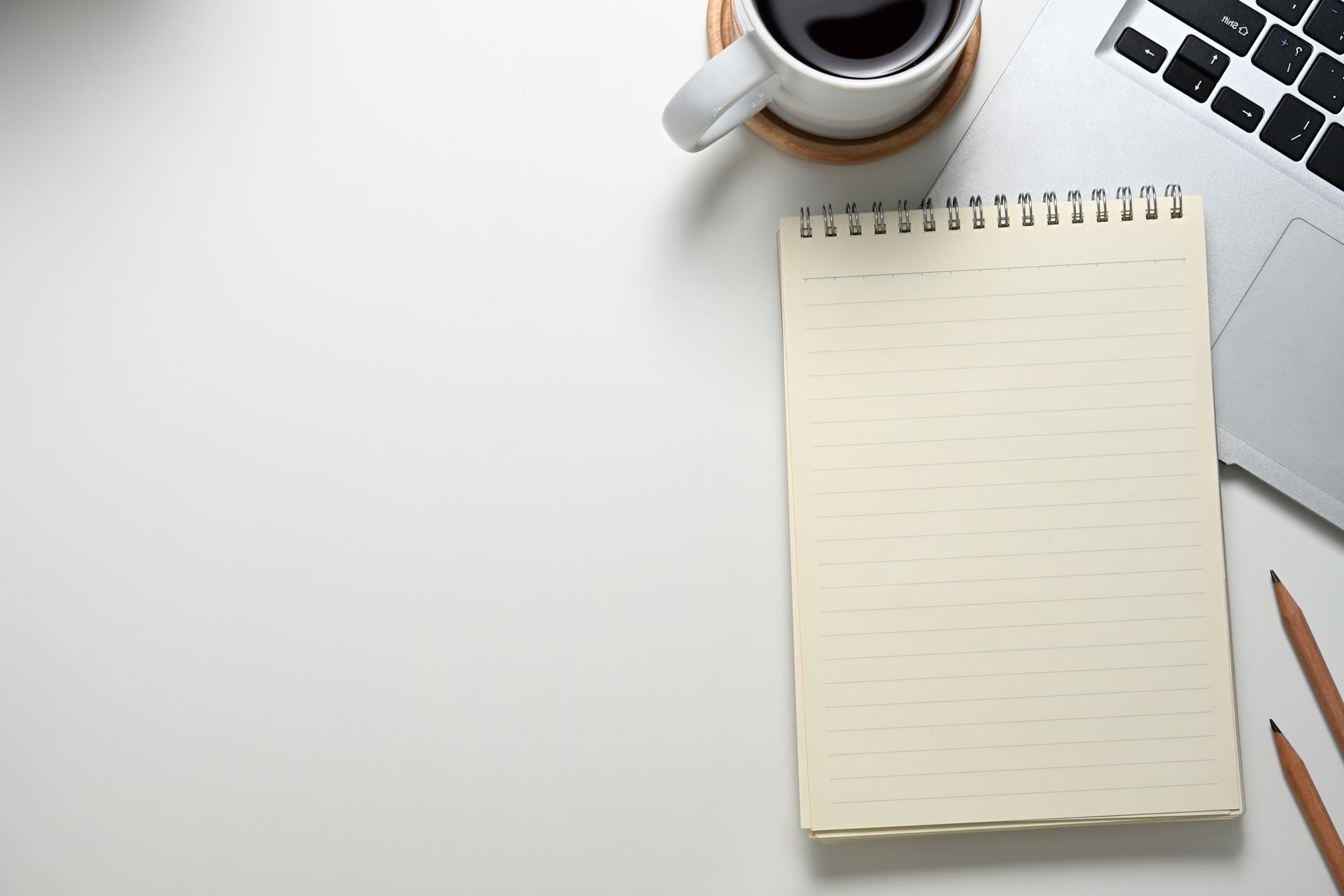 White desk with coffee, notepad, pencils, and laptop.