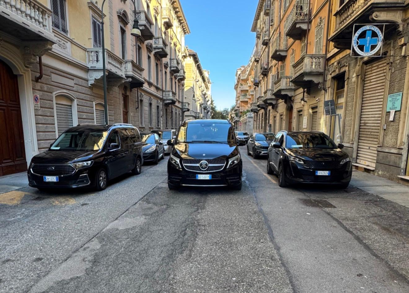 Tre furgoni di lusso neri parcheggiati in una strada stretta tra edifici storici a più piani in una città.
