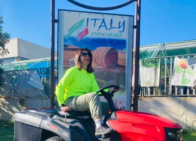 Una donna su un trattorino rosso sorride davanti a un cartello con la scritta 