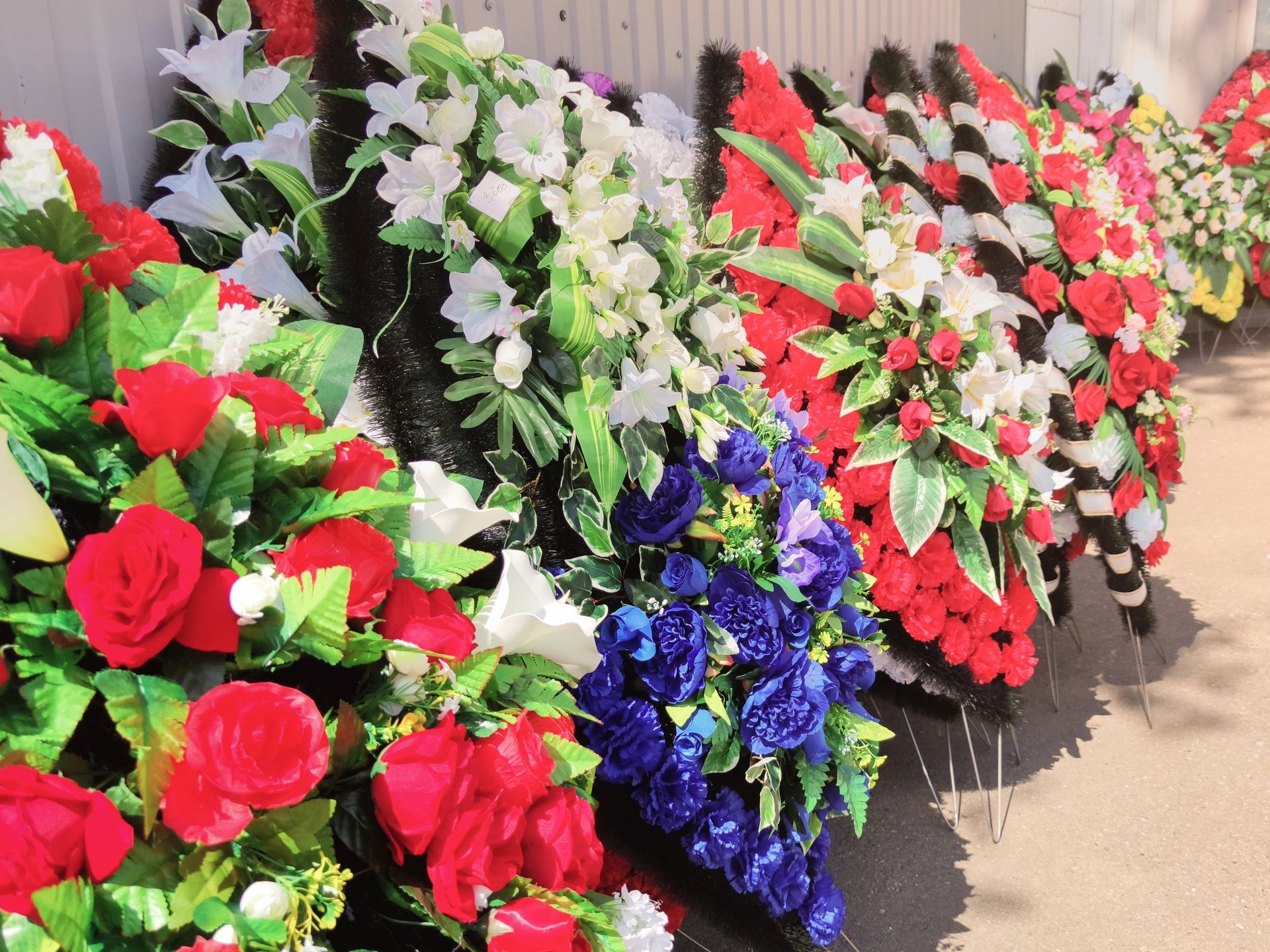 Ghirlande di fiori artificiali colorati, tra cui rose rosse e gigli bianchi, disposte in fila.