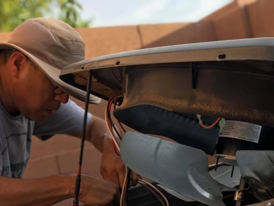 a man wearing a hat is working on an air conditioner .
