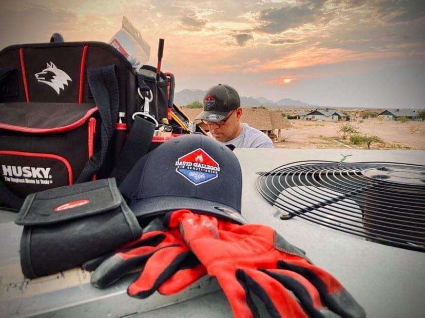 a man is working on an air conditioner next to a hat and gloves .
