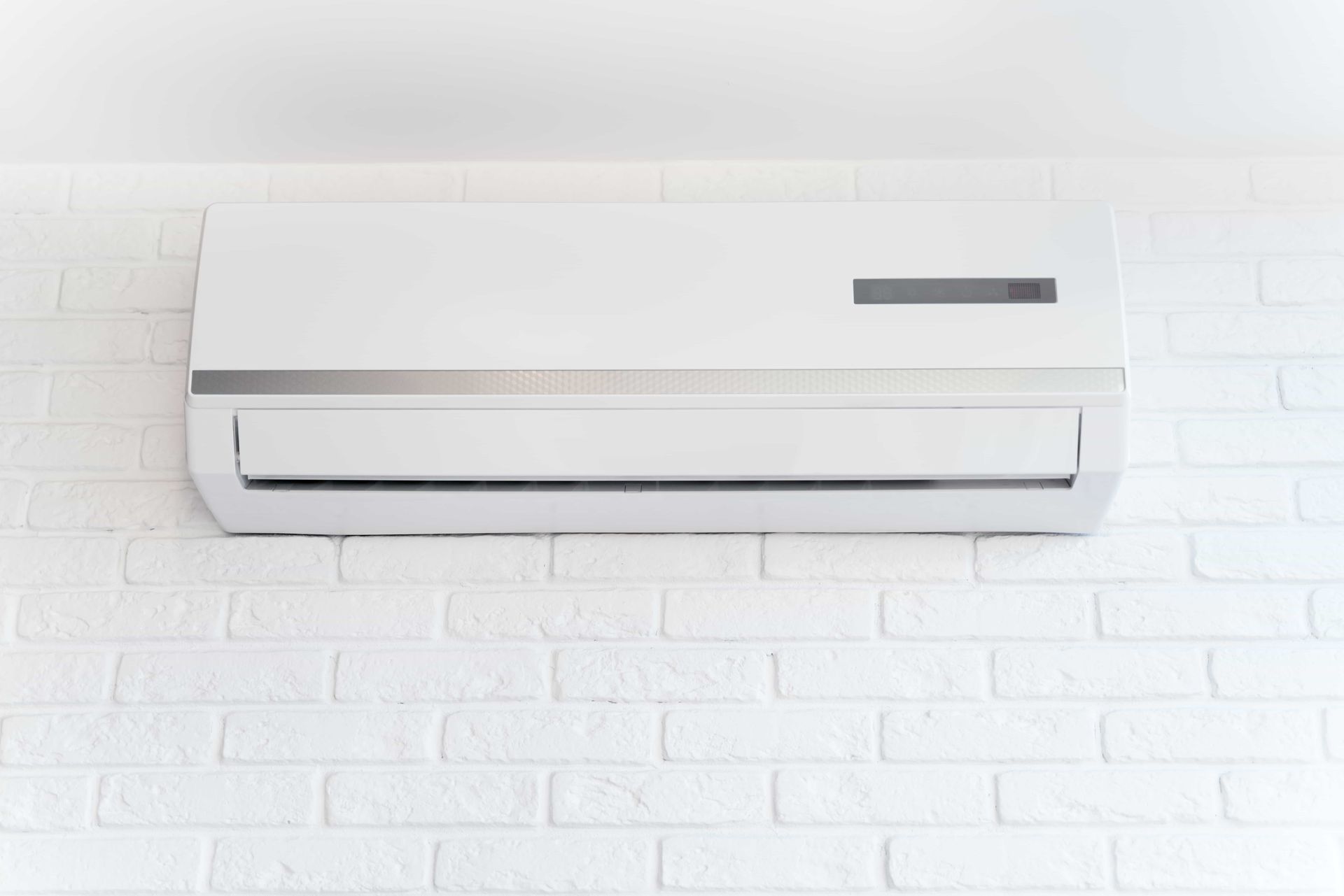 a white air conditioner is hanging on a white brick wall .