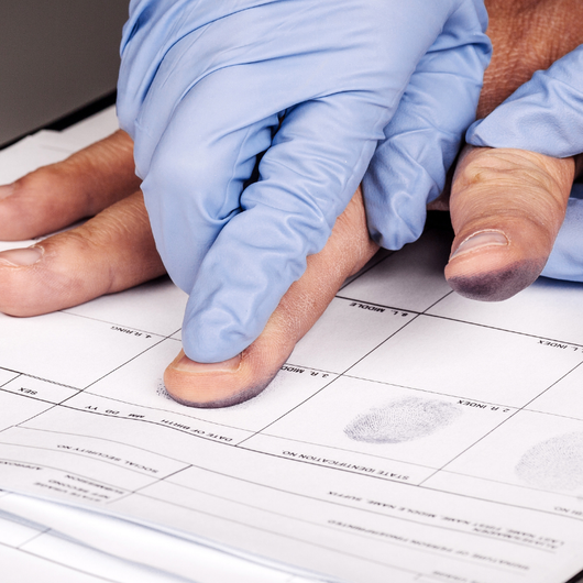 A person wearing blue gloves is touching a fingerprint on a piece of paper