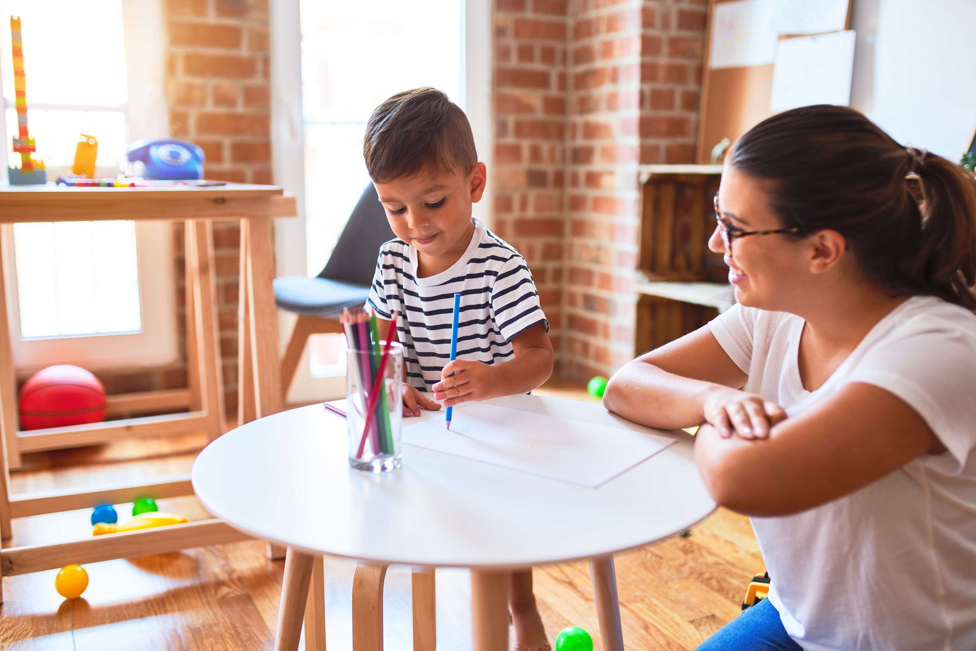A woman and a child are sitting at a table drawing with markers
