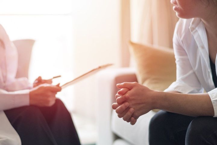 A woman is sitting on a couch talking to a doctor