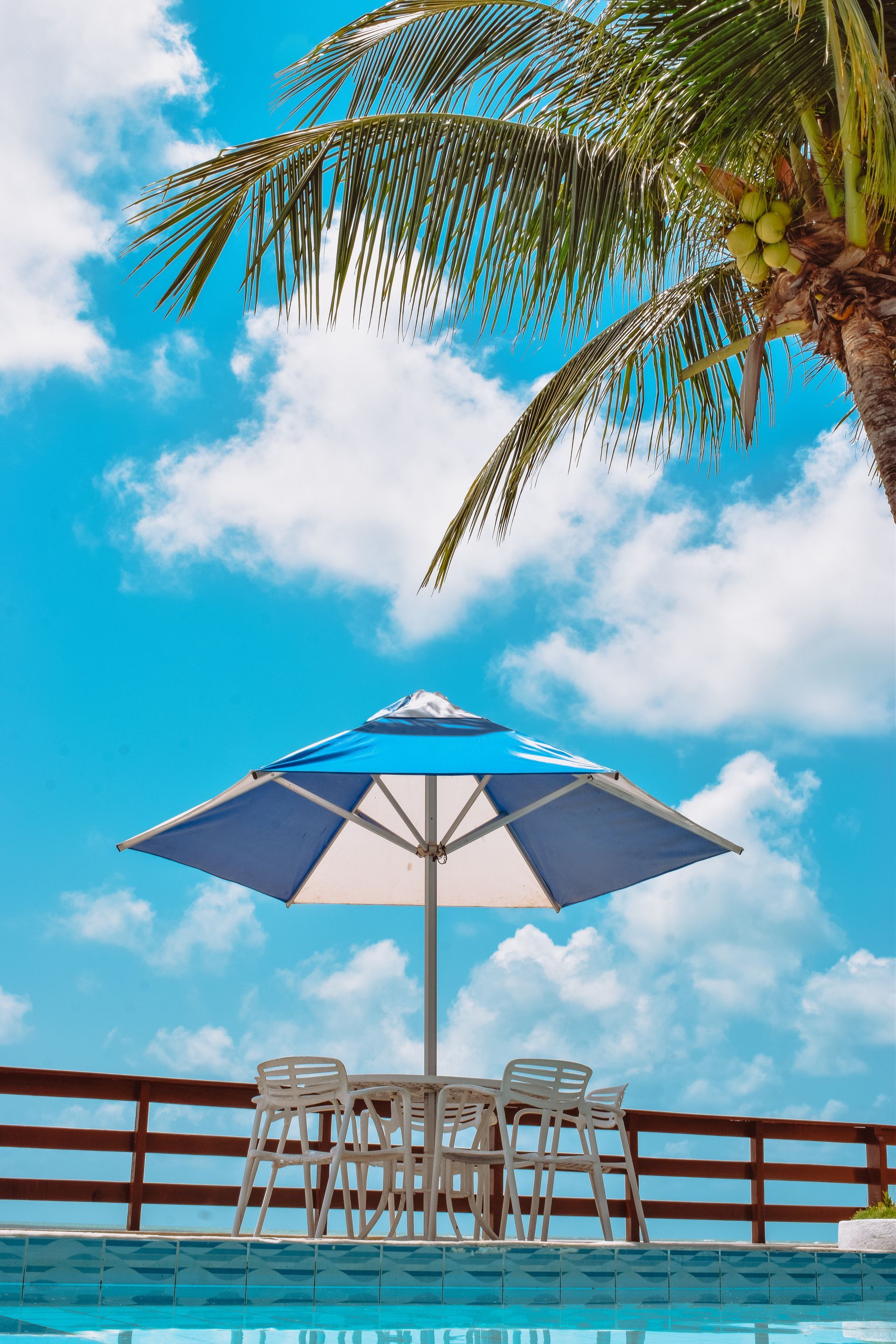 A table and chairs under an umbrella next to a swimming pool.