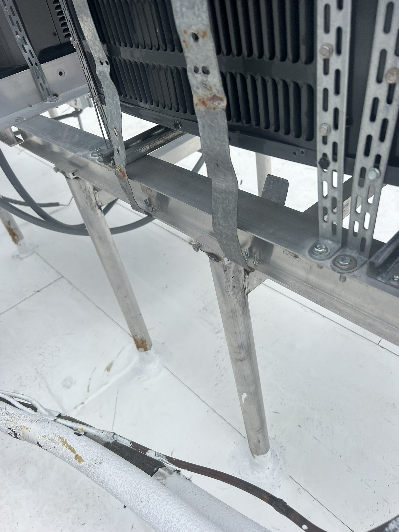 Solar panel support structure on a white roof, with metal legs and electrical cables.