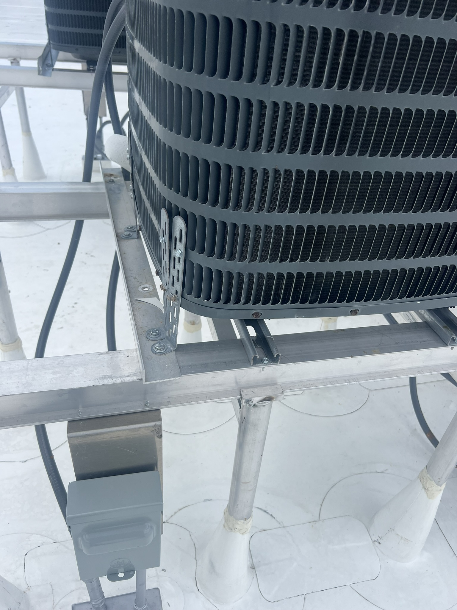HVAC unit on a roof, with metallic frame support, electrical box, and white roofing.