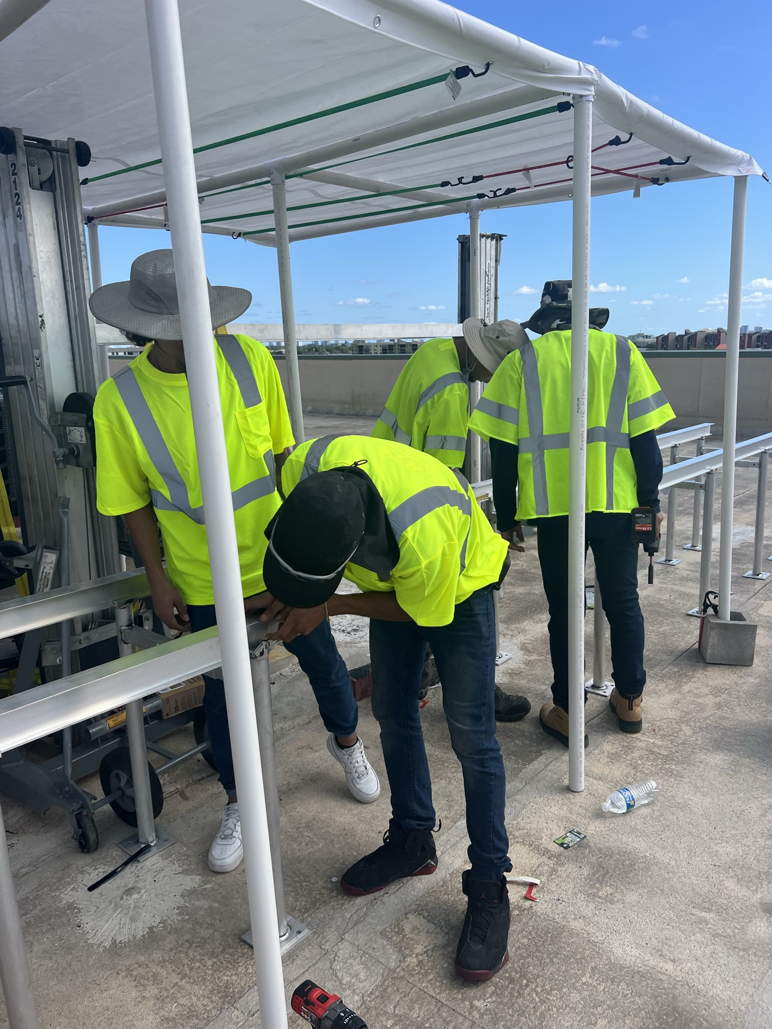 Construction workers in reflective vests install a structure on a rooftop under a blue sky.