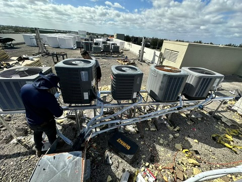 Workers installing AC units on a rooftop. Gray, black units sit on metal scaffolding.