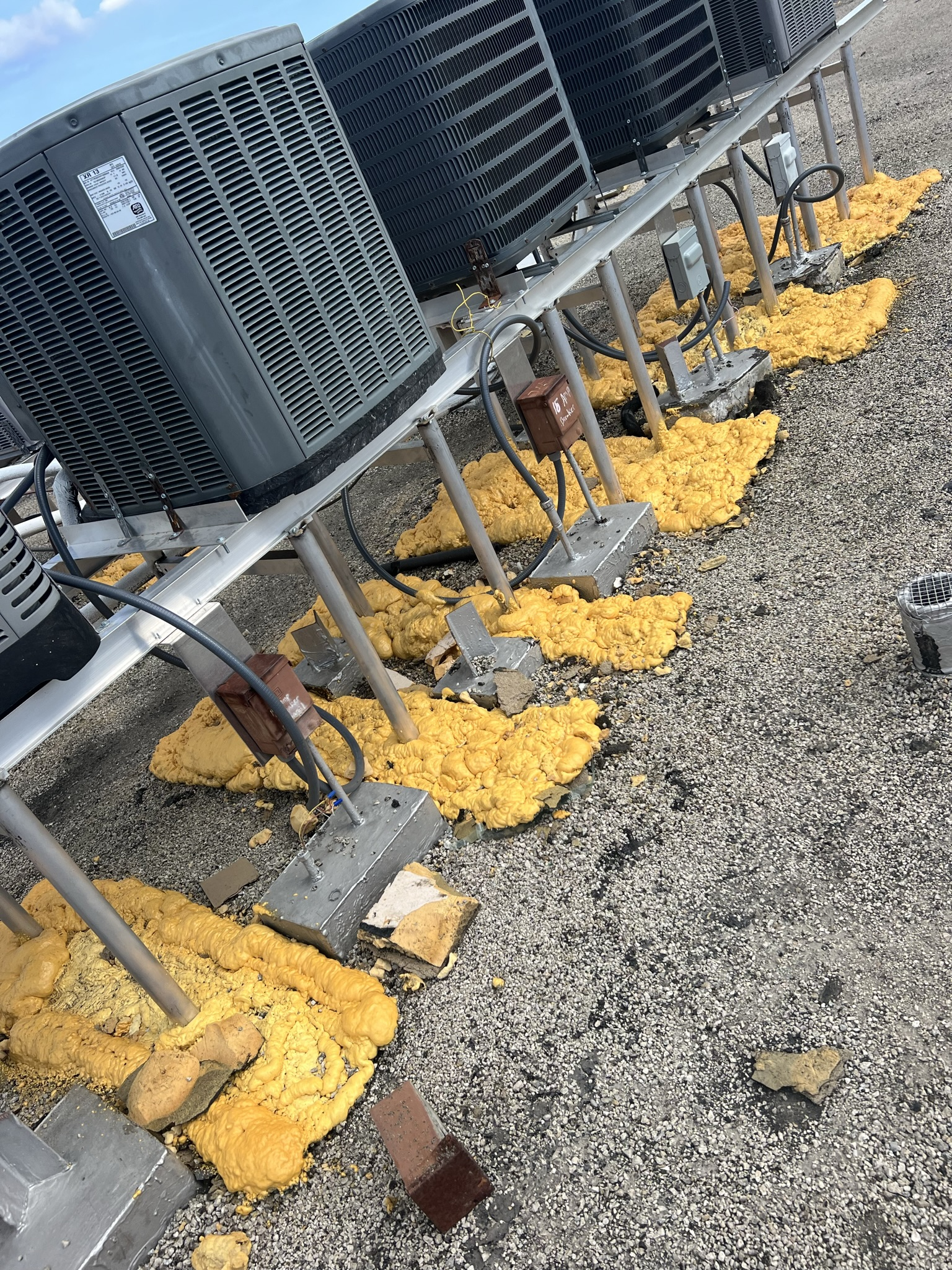 AC units on a rooftop, supported by yellow foam pads. Gravel covers the roof.
