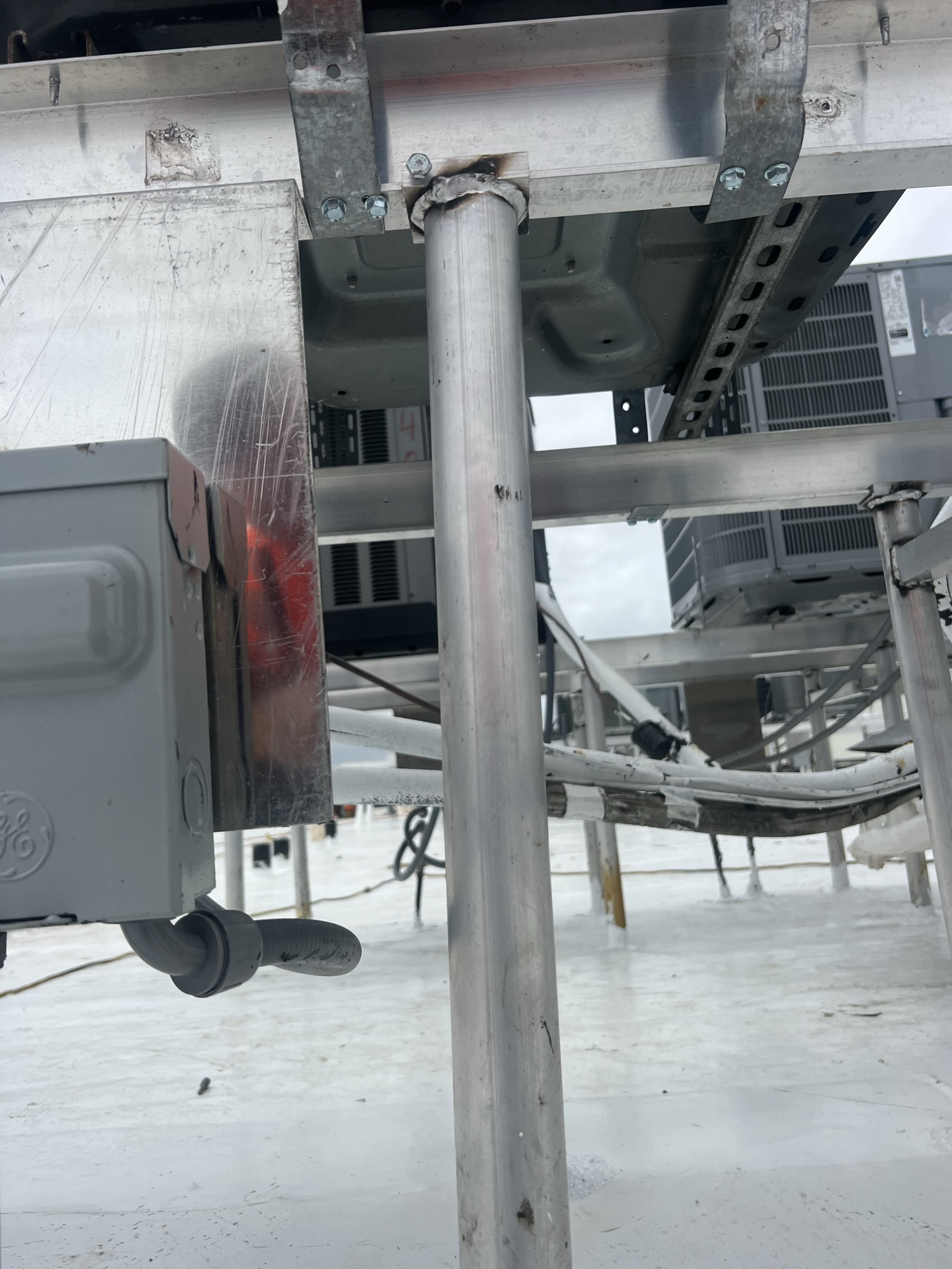 Metal pole extending from a rooftop, supporting other equipment. Gray electrical box and framework visible.
