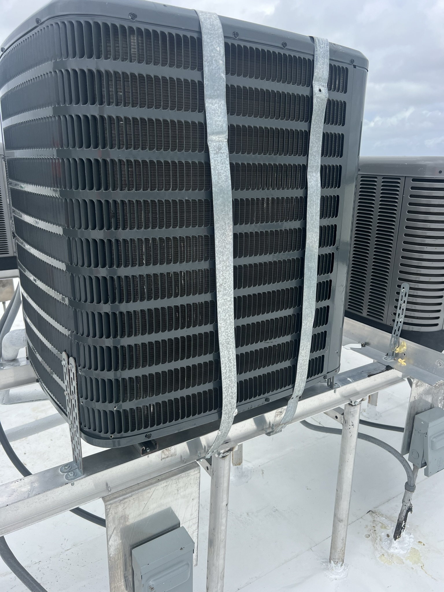 HVAC unit on a rooftop, secured by metal straps.