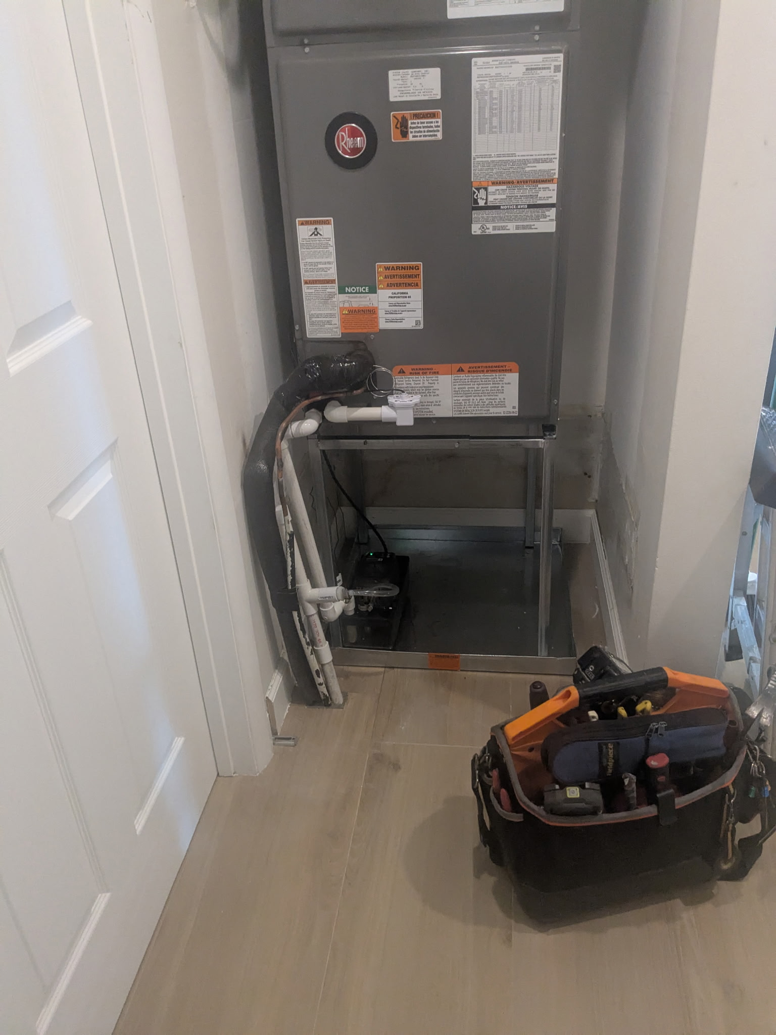 HVAC unit in a closet. A tool kit is in front. White doors and light wood flooring.