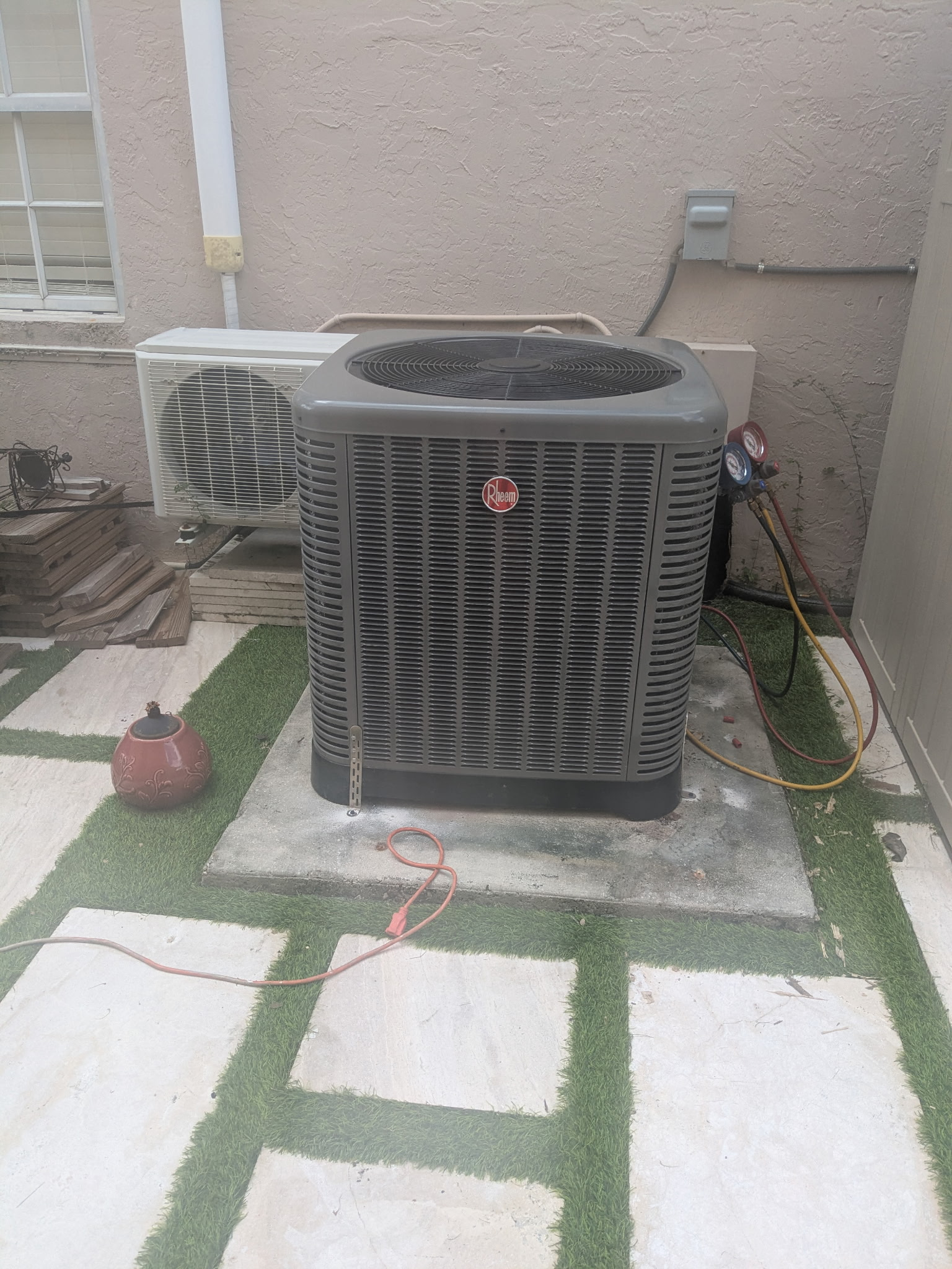 An air conditioning unit on a concrete pad outside a building. Hoses are attached.
