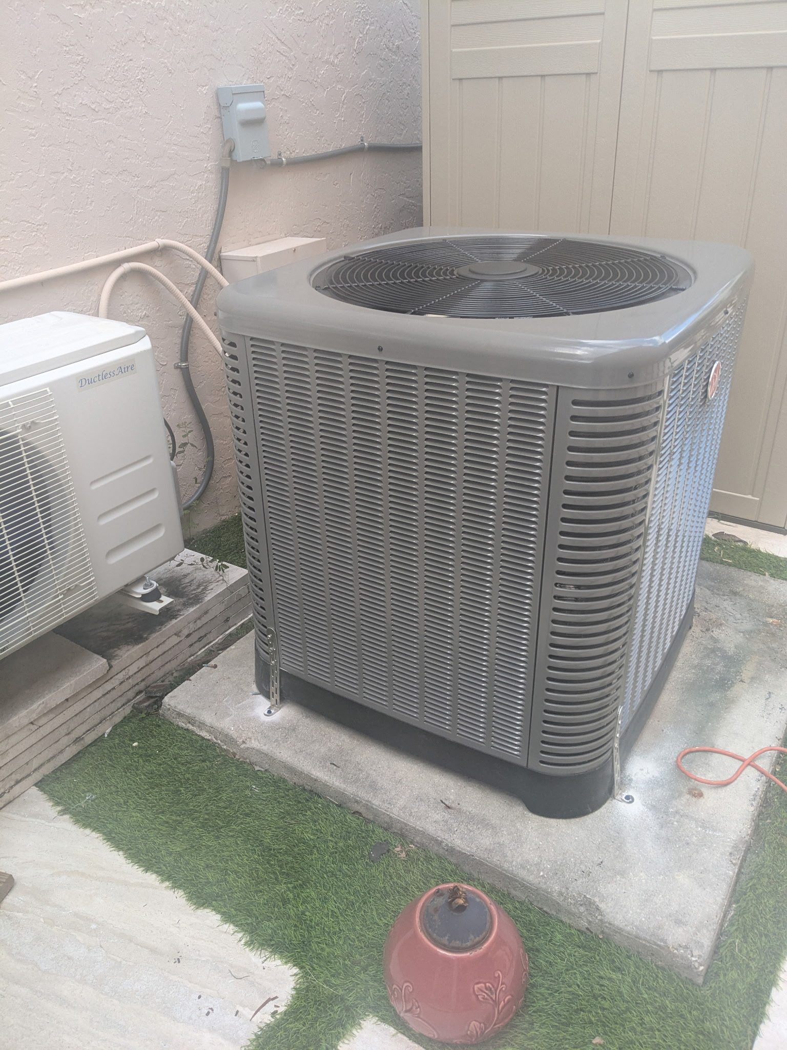 AC unit on concrete slab next to a building, with another white unit and grass visible.