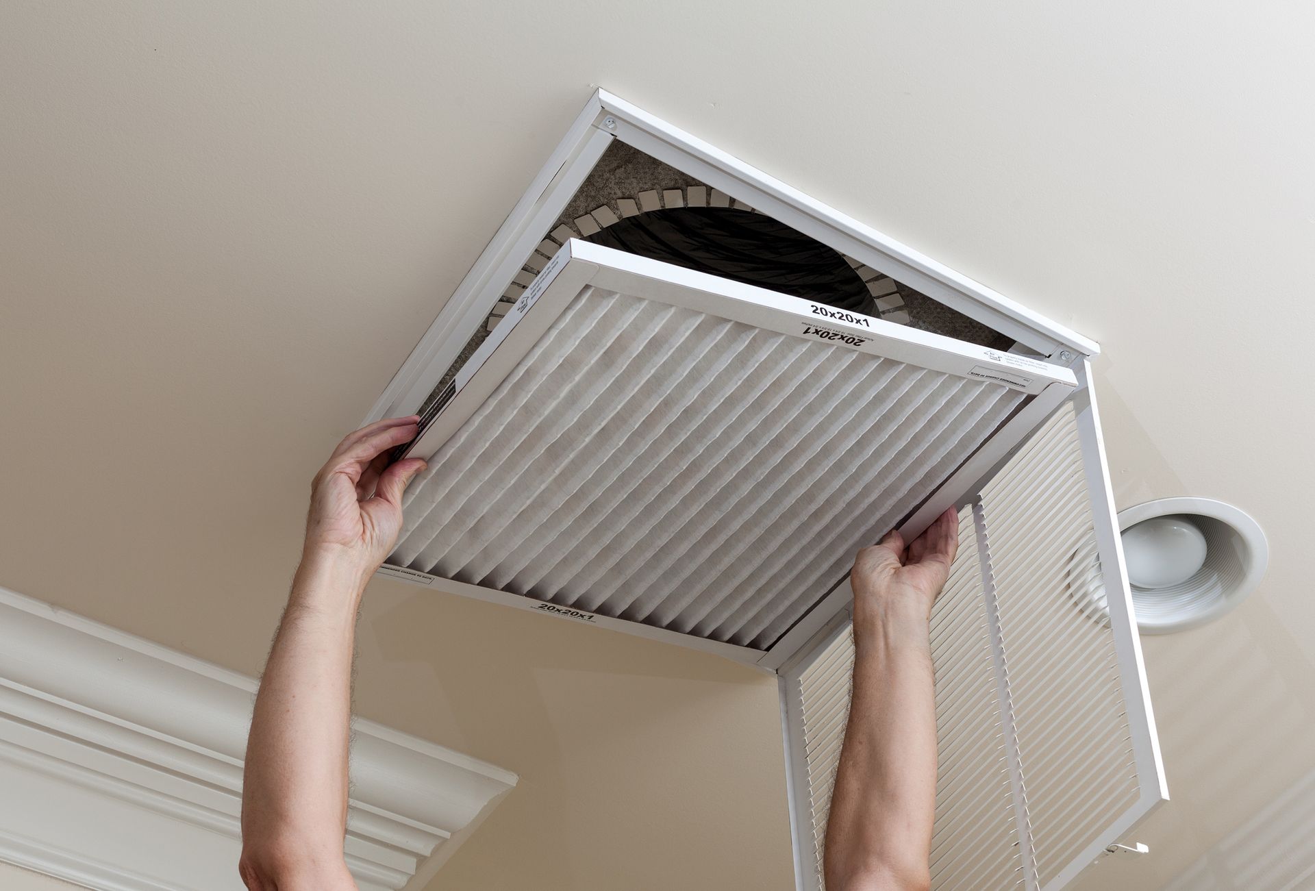 Person replacing an air filter in a ceiling vent.