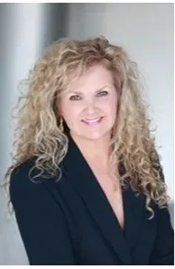 A woman is sitting at a desk with a laptop and a vase of flowers.