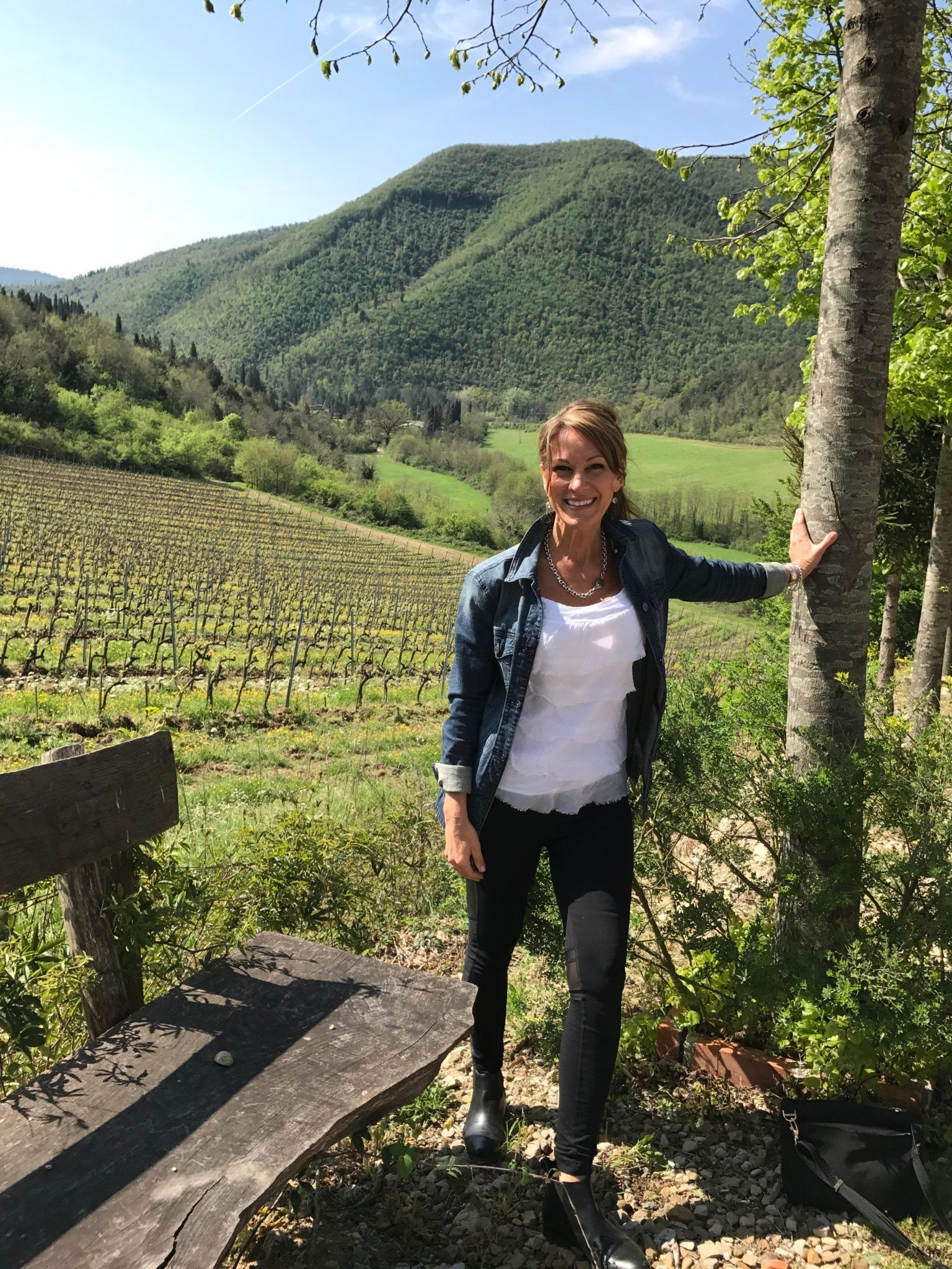 A woman is standing next to a tree in a vineyard.