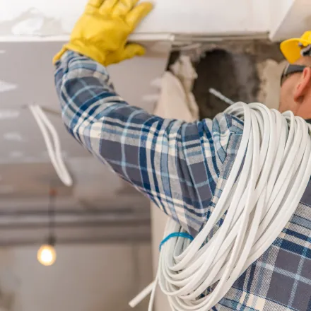 Grounded Electric - A man wearing a plaid shirt and yellow gloves is working on a ceiling