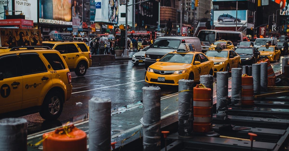 A row of yellow taxis are driving down a city street on a rainy day.