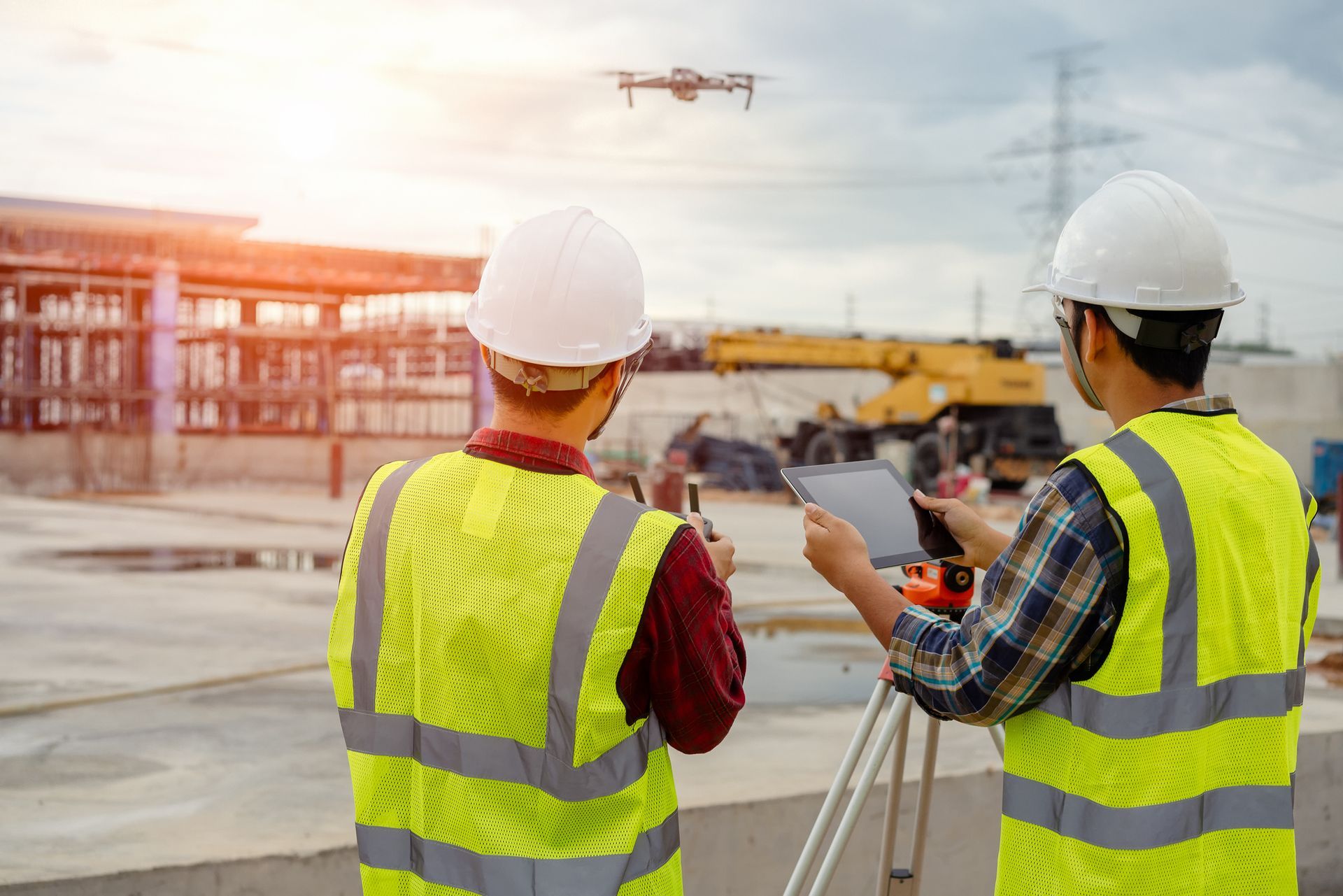 Two construction workers are looking at a drone on a construction site.