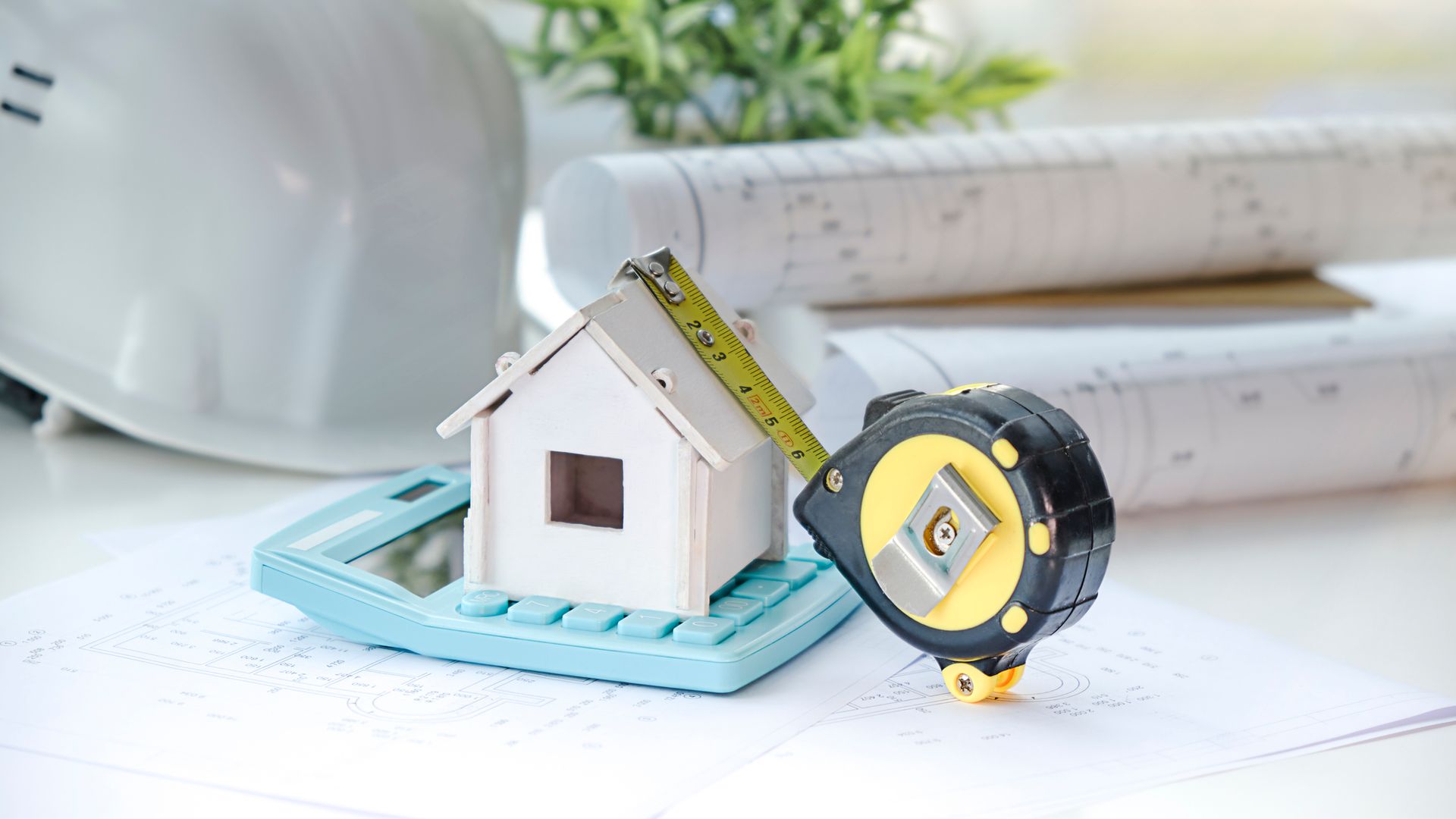 A small house is sitting on top of a calculator next to a tape measure.