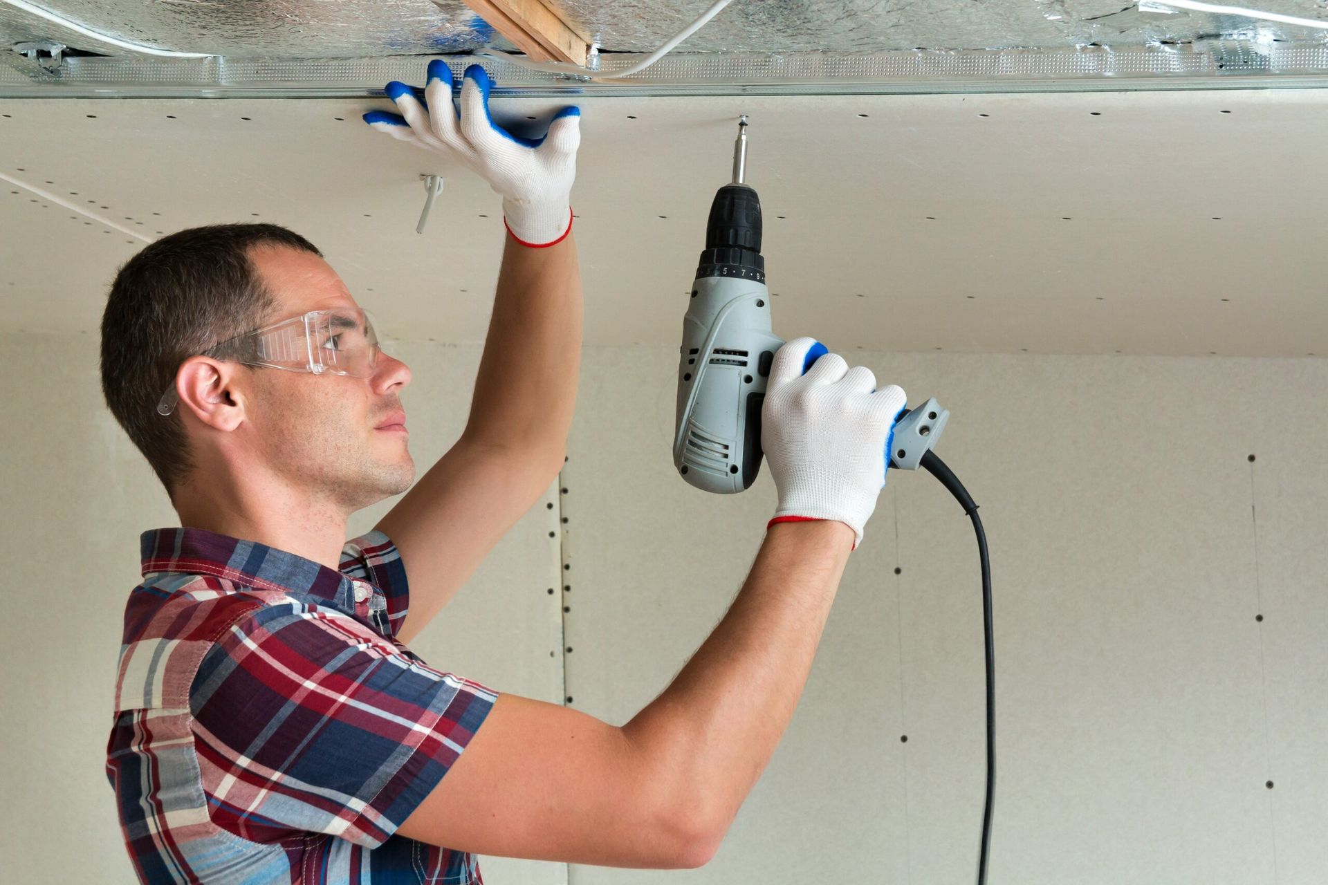 A man is using a drill to drill a hole in the ceiling.